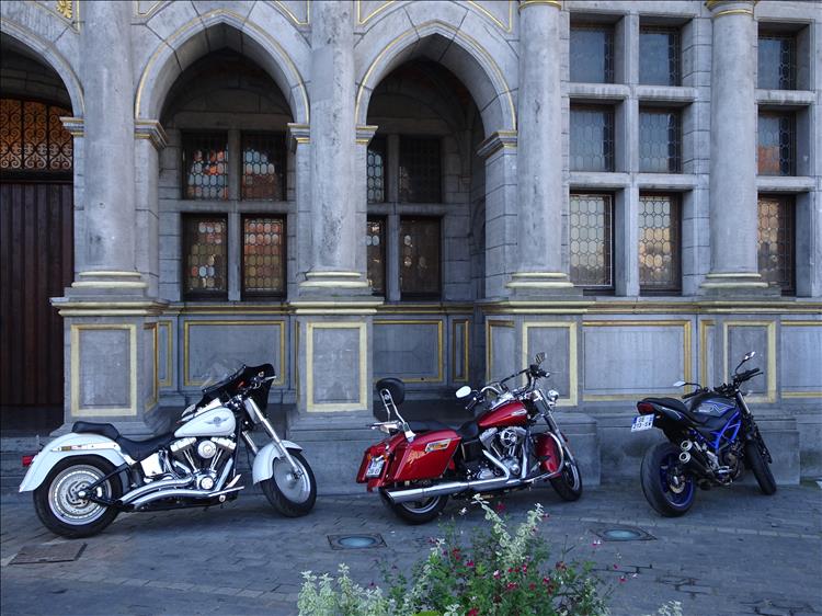 3 motorcycles, 2 of them harleys the other a street bike, outside a grand building