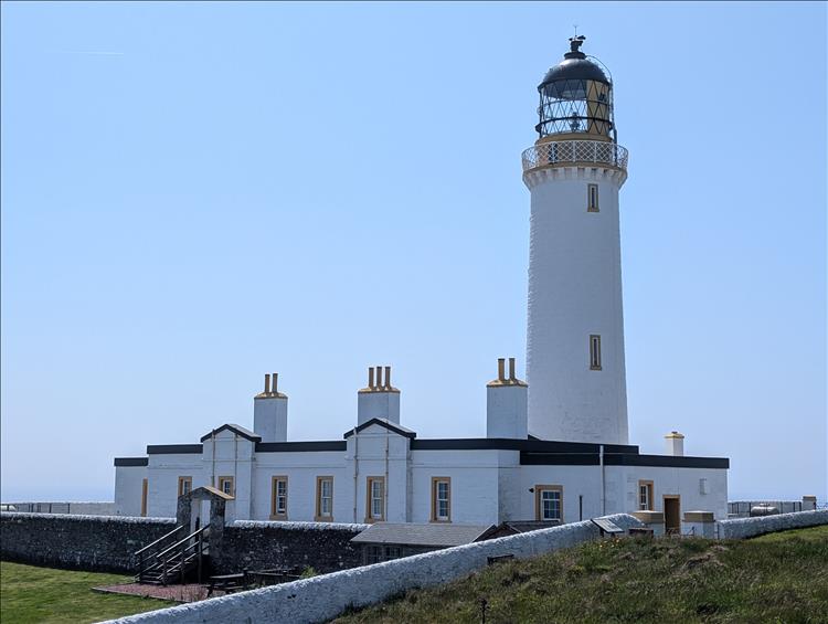 A tall crips white painted lighthouse and associated buildings all fresh and bright in the sun