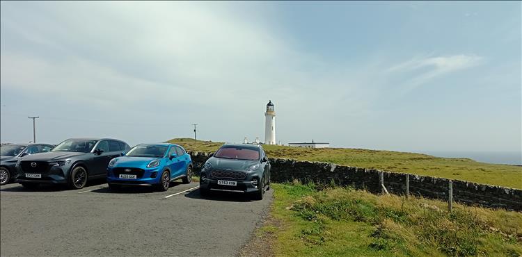 The lighthouse pops over the stone wall and car park at the tip of the promontory