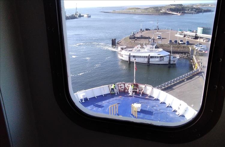 Through the window we see the port and the bow of the ship. 2 men are painting the deck just behind the bow