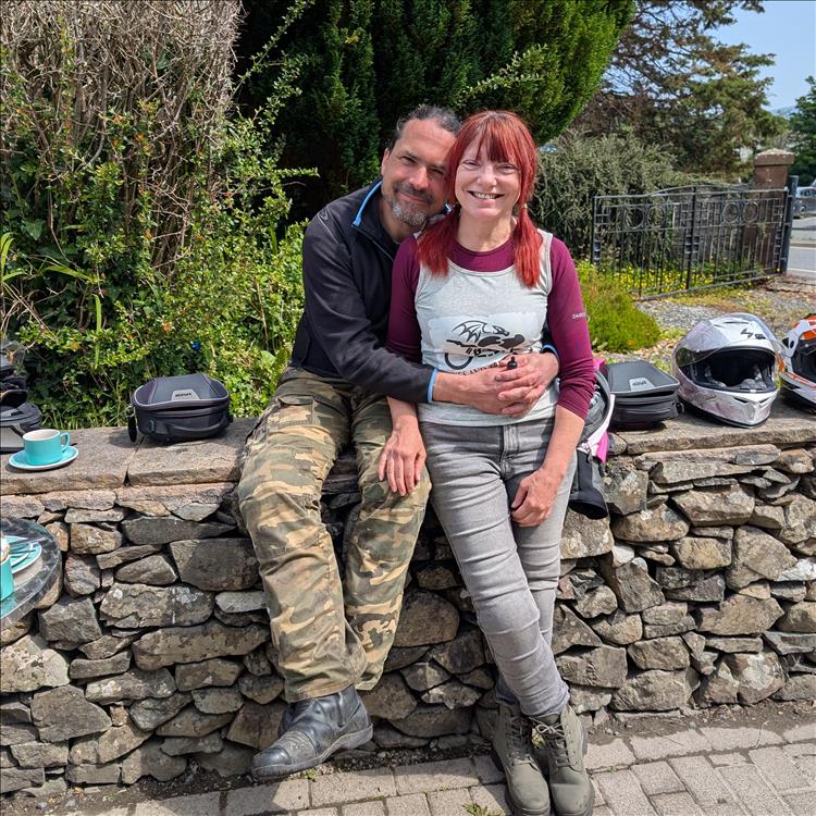 Ren has his arms around Sharon outside the cafe in the sunshine, both smile for the camera