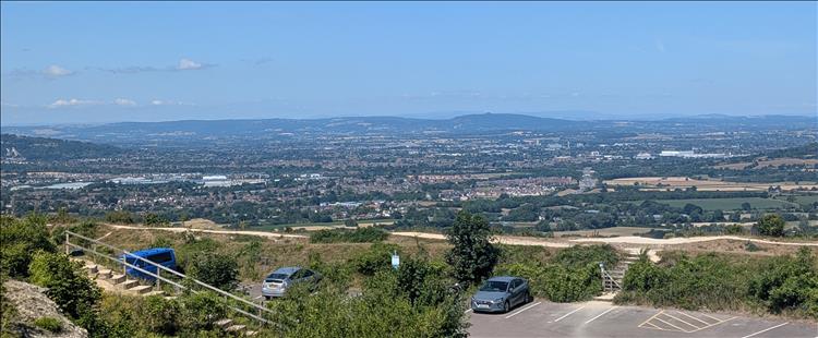 From atop a big hill we see a vast plain with trees and towns and hills in the far distance