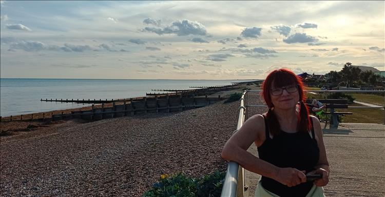 Sharon smiles in the setting sun beside the sea and posh houses along the coast in Ferring
