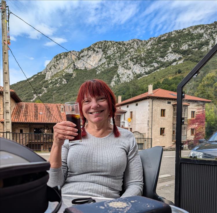 Sharon smiling with a drink of pop with the houses and hills behind her