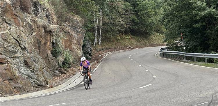 A cyclist whizzing down a road beside mountainous rocks and safty barriers