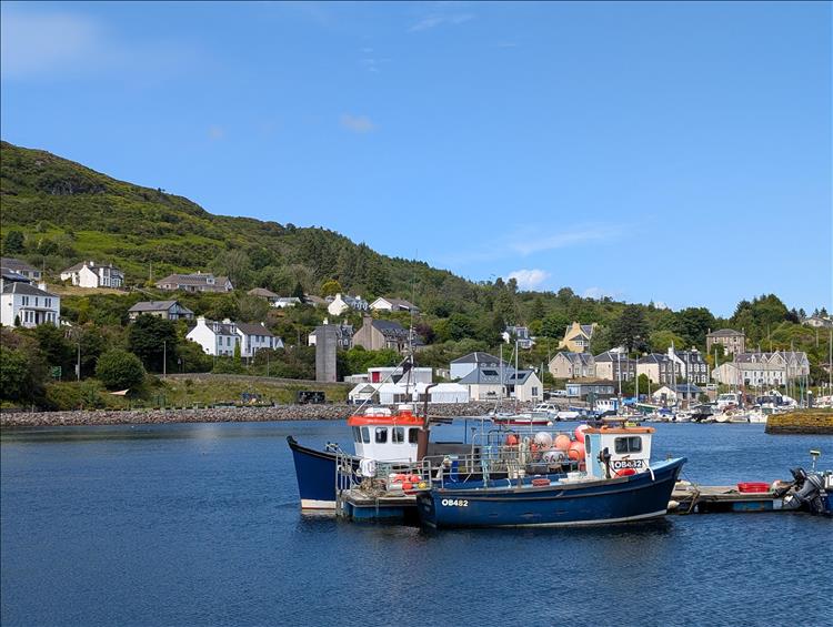 A couple of small fishing boat in the calm waters of Tarbert Harbour, a few houses, hills and glorious weather