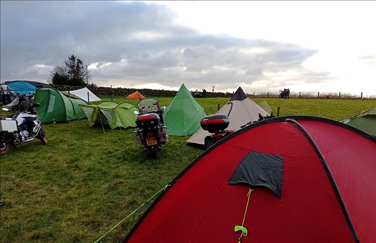 A number of tents and a few motorcycles in a field under skies that are turning grey