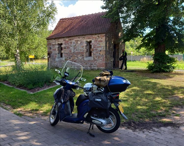 A tiny church not much larger than a car garage in the trees, there's a scooter out front