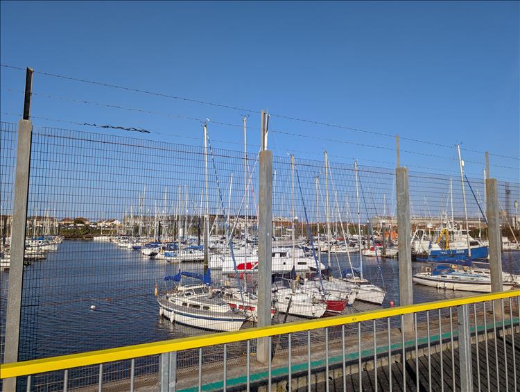 Looking through wire fence we see plenty of sailing boats in the harbour and sunshine at Troon