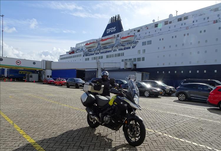 Upt's wife stands by the 650 VStrom with the large ferry behind them at the port