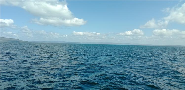 Looking out over calm sea loch waters there's light cloud and hilly shorelines in the far distance