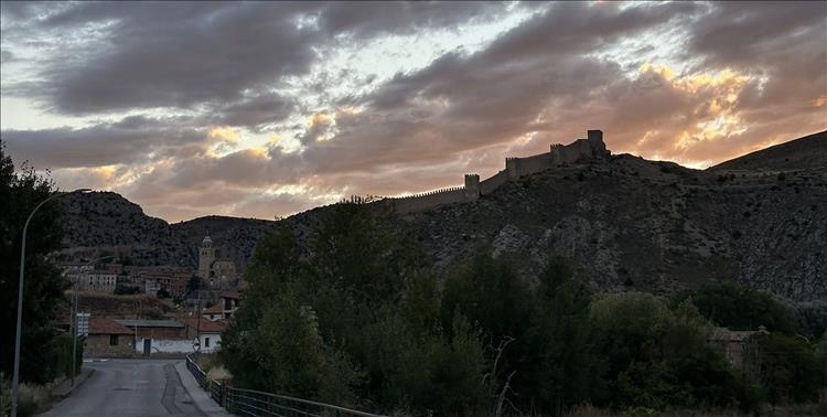 A road leads into the town, behind we can make out a castle against the fading light 