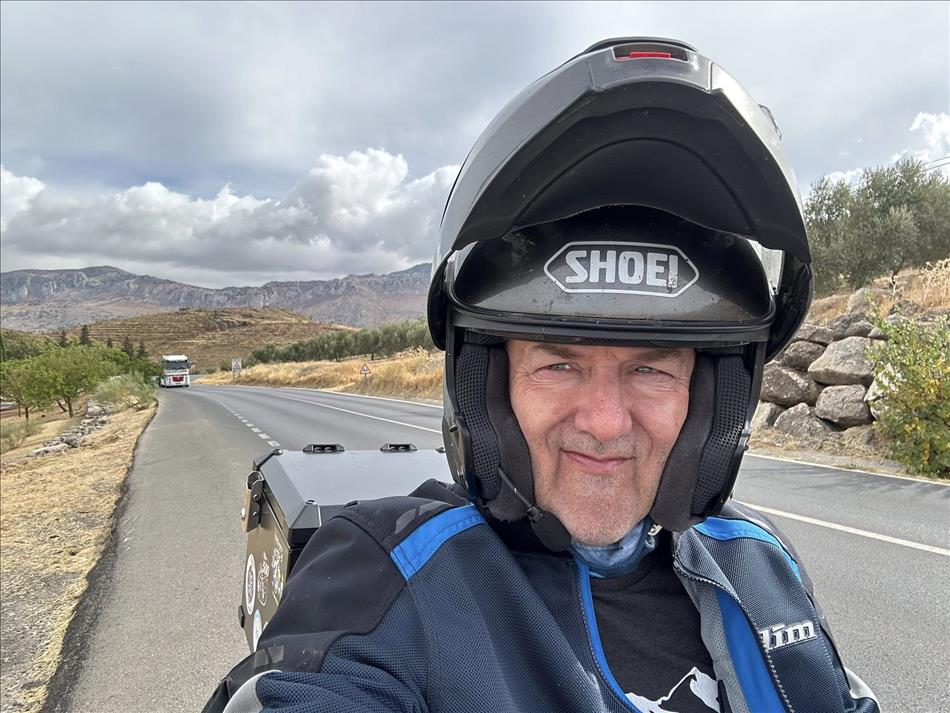 Selfie of Andy on the bike with his flip front helmet open and the spanish mountains