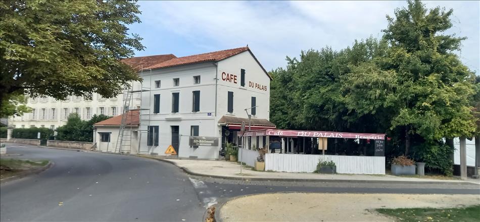 A long french building with a covered eating area outside by the trees