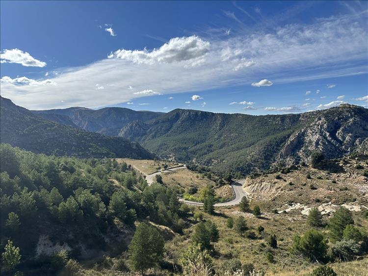 A road curves sharply though valst huge mountain scenery with bushes and dry land and rocks