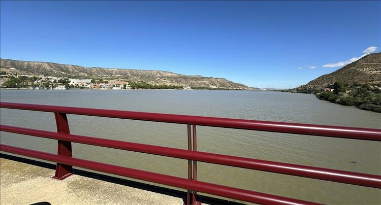 A vast wide flat river with towns on the banks and hills in the distance, blue skies