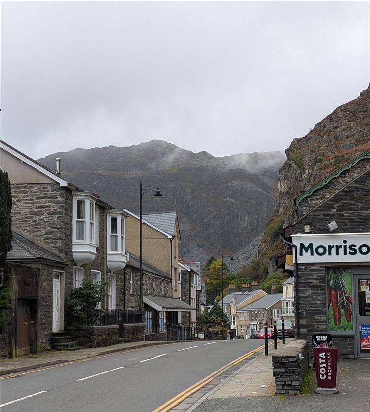 A street with houses, dominated by vast towering rock formations and mist