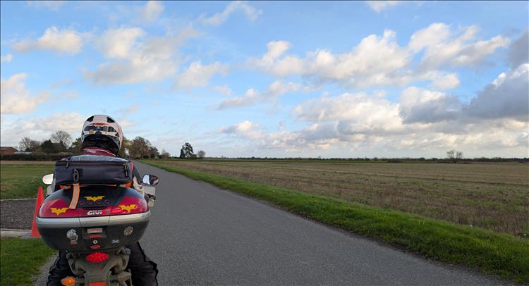 Flat road, flat fields and Ren on his bike seen from the back in Lincolnshire