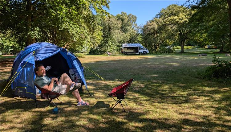 Ren sits on a camping chair outside the tent in good weather just chilling out