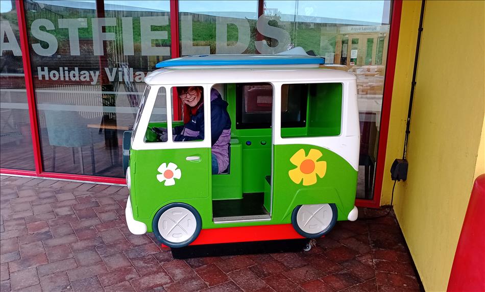 Sharon inside a tiny little plastic van that a child rides in, smiling and looking very silly