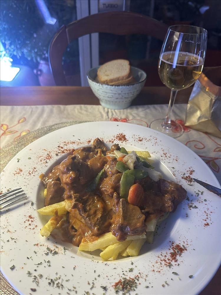 Meat and veg stew on chips, the plate and a glass of wine