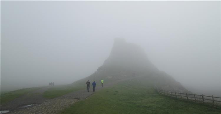 A path in very thick mist, people walking up to what looks like a lump in the mist