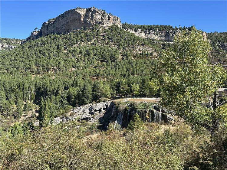 Massive towering rocks, trees, a valley and a broad rocky waterfall