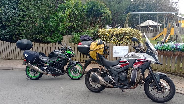 Both bikes still with luggage beside a playground and smart wooden fencing at the caravan site
