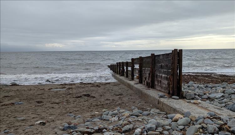 Old, rotten wooden planks and rusted steel form groynes into the sea on beach