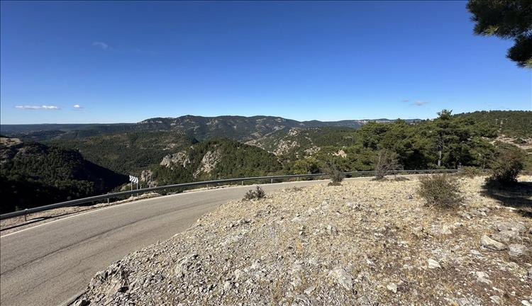 A curve in the road with a barrier, beyond and endless range of mountains and blue skies