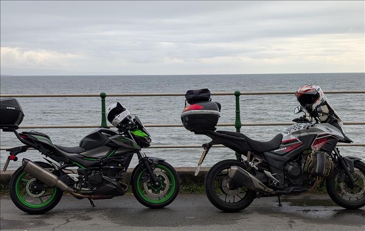 The CB500X and Z500 beside the railings with the sea stretching away behind