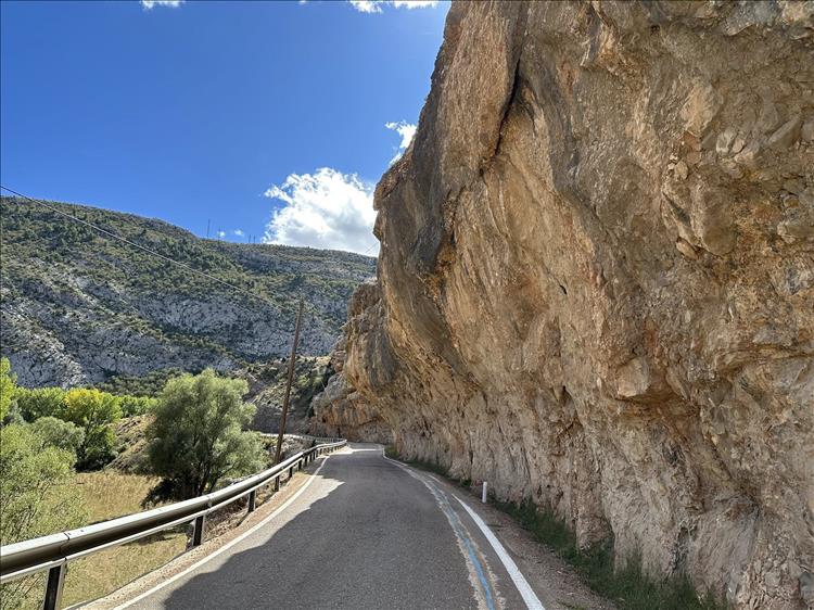 Sand coloured rocks overhang closely a narrow road underneath them