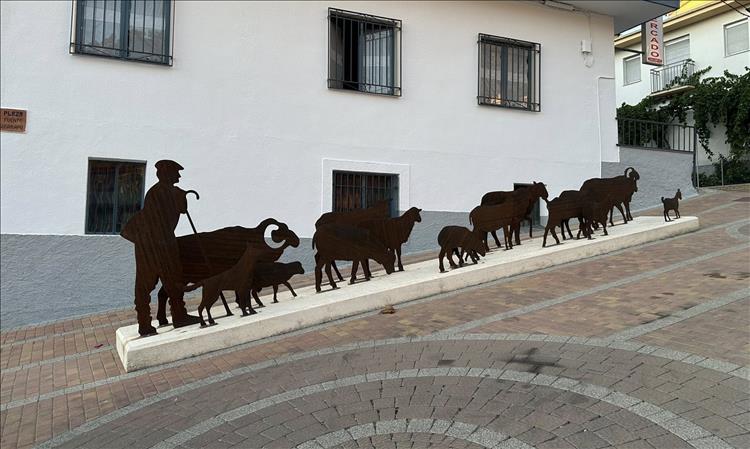 A steep street in a town, with an art piece outline of a shepherd and several sheep climbing the steep lane