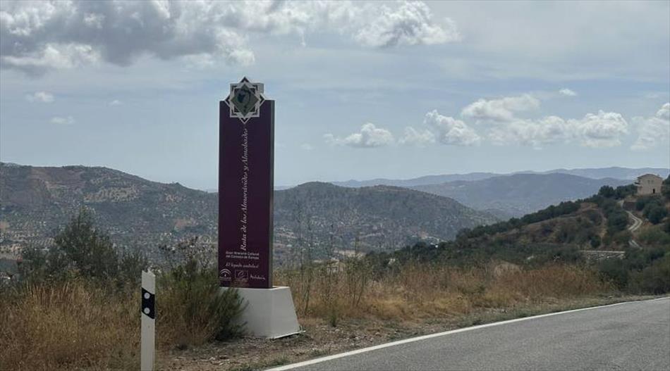 A long tall dark red signs with writing on it beside the road