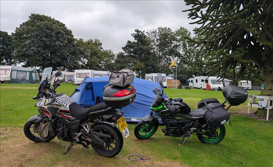 The bikes, the tent behind on the grassy area surrounded by trees at the campsite