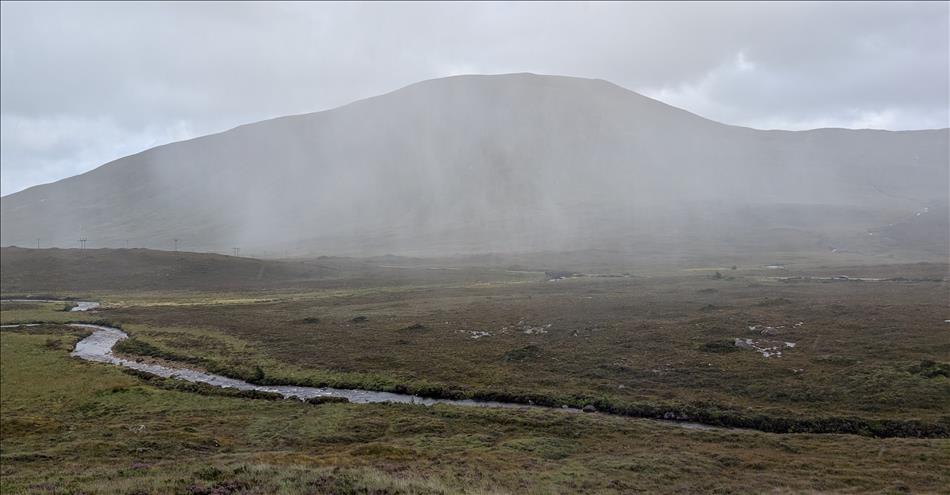 Vast flat river bed with hugh mountain behind, we can see the torrential rain coming down