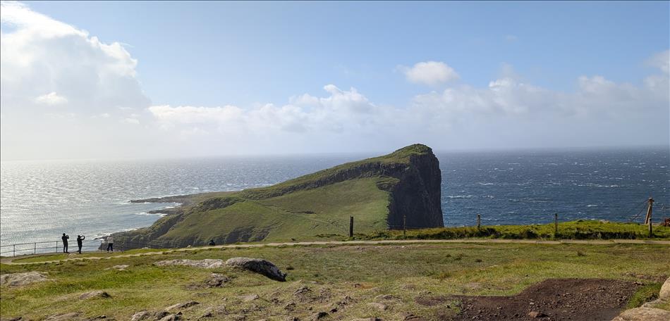 An agled sloped promentory juts out into the sea, clouds and sky