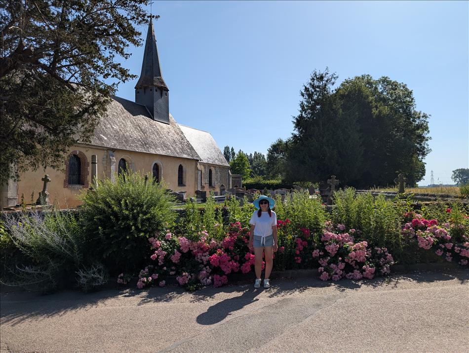 Sharon in shorts outside the church amid blooms and flowers and trees and sunshine