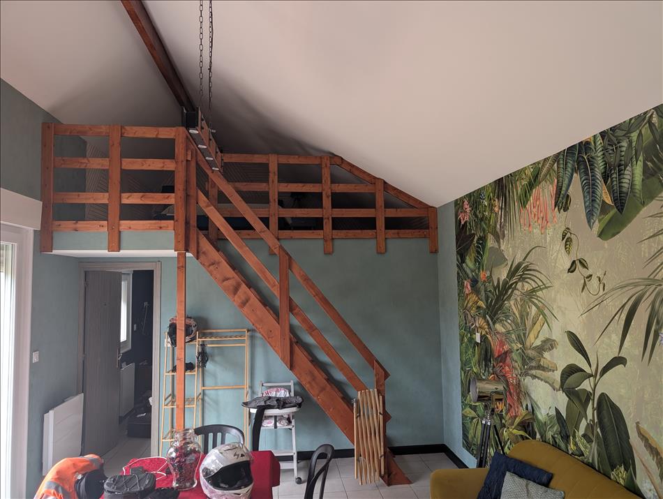 A tall room with a mezzanine floor in the apex of the roof, below a bedroom and then tables and chairs