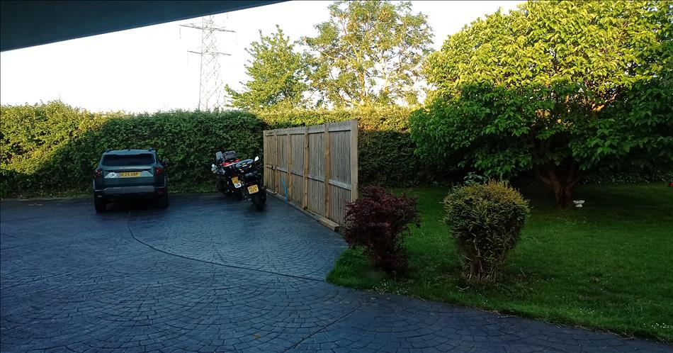 2 motorcycles and a car shadow as the sun rises over the trees, bushes, garden, and driveway