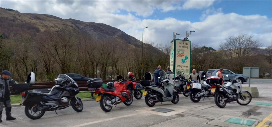A few motorcycles beside the large Green Welly sign with the delightful Highland scenery behind