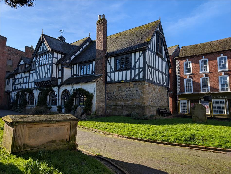 A tudor timber framed building painted black and white, Regency brick house behind