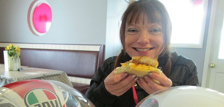 Sharon smiles broadly and shows the camera her half eaten egg barm at cafe fresh