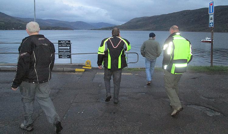 4 chaps in bike gear walking around in Ullapool overlooking loch broom