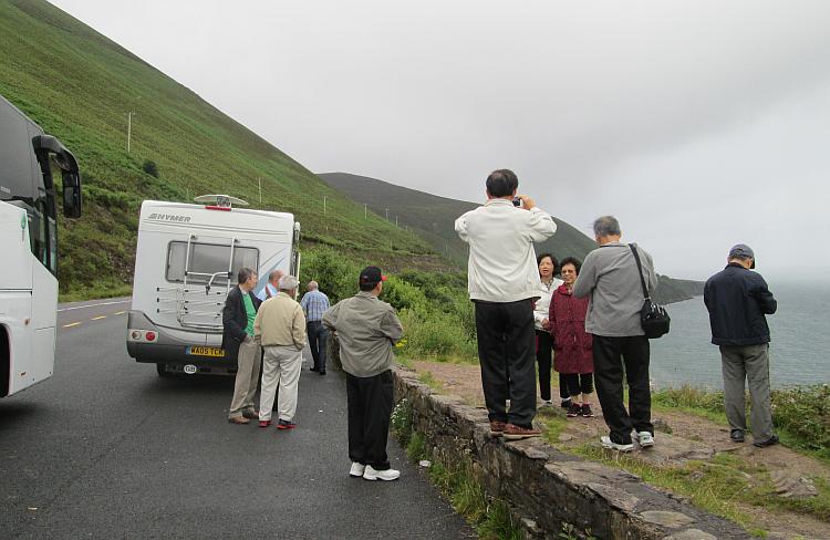 Oriental tourists, the campervan and coach overlooking a bay in Ireland