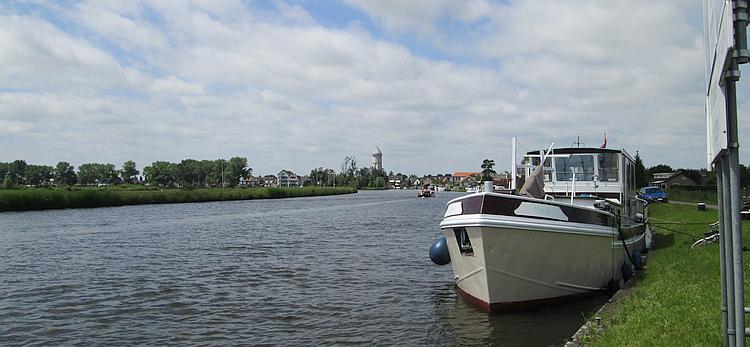 A broad river or canal, a boat and open countryside and trees in The Netherlands