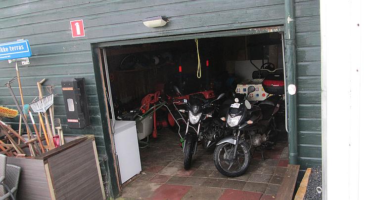 The 2 bikes parked in the garage next to the small tractors