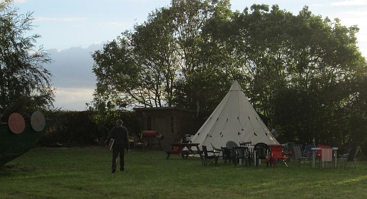 In a field there's a small shed, a large teepee and plenty of chairs
