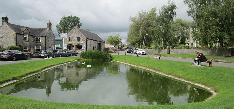 Hartington's small pond with 2 white ducks upon it, surrounded by quaint stone cottages