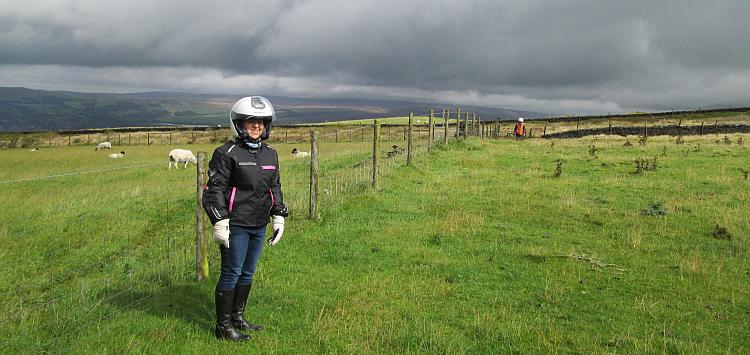 Paula stand on a windswept hill as grey clouds form above.